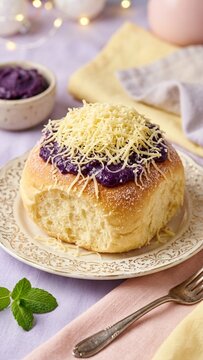 Filipino ube ensaymada brioche bun topped with grated cheese on decorative plate with pastel background