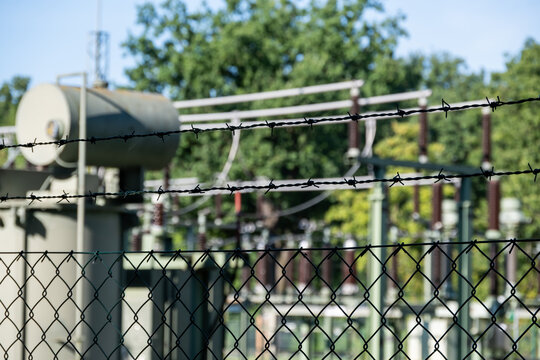 Detailed view of a high-voltage electrical substation secured behind a robust chain-link fence and barbed wire, highlighting critical infrastructure protection.