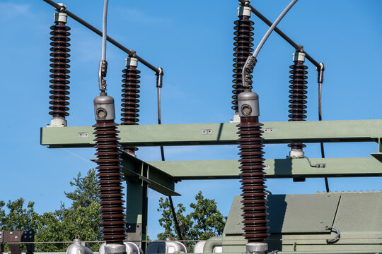 Detailed view of high-voltage insulators and electrical infrastructure components in a substation against a clear blue sky, showing power distribution and industrial engineering.