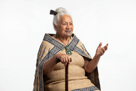 Elderly maori woman with traditional moko kauae tattoo wearing woven cloak holding walking stick speaking with hand gesture cultural heritage and indigenous wisdom