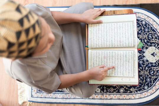 Overhead perspective showcases exceptional religious discipline as a devoted student analyzes sacred scripture upon a traditional rug reflecting pure cultural heritage and wisdom