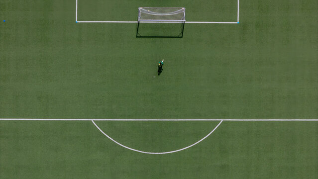 Aerial view of a lone soccer player standing on a green artificial turf field with white markings in front of a goal in Gdansk, Poland.