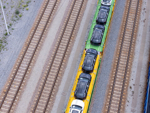 Aerial view of a freight train transporting new black and white cars on flatbed wagons along railway tracks in Gdansk, Poland.