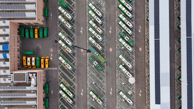 Aerial view of an electric bus depot with rows of parked buses and solar panel installations on facility rooftops in Milan, Lombardy, Italy.