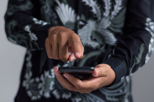 Close up of hands in batik shirt tapping on black smartphone screen, embodying direct digital engagement, smart cultural access, asian fintech action, and mobile connectivity