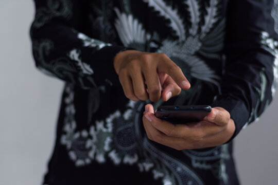 Close up of hands tapping smartphone screen in batik clothing, symbolizing active digital transaction, seamless cultural fintech, precision screen navigation, and mobile connectivity