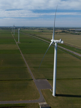 Aerial view of wind turbines standing in a vast green agricultural landscape under a blue sky in the Netherlands.