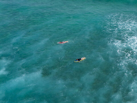 Aerial view of two surfers paddling on their surfboards in the clear turquoise water of Nusa Dua Beach, Kecamatan Kuta Selatan, Bali, Indonesia.