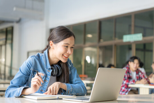 Beautiful Asian woman female student excited checking language test results on laptop. Smile girl happy study online. book in college campus. Portrait female on international Asia University.