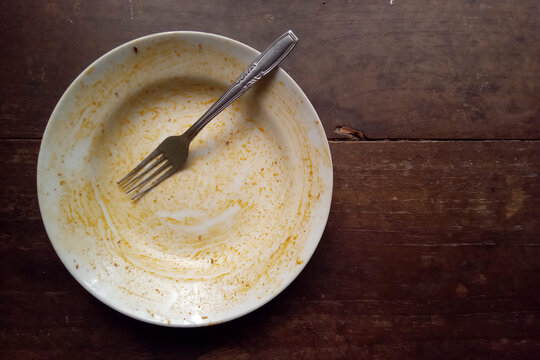 Empty plate rests on dark wooden surface