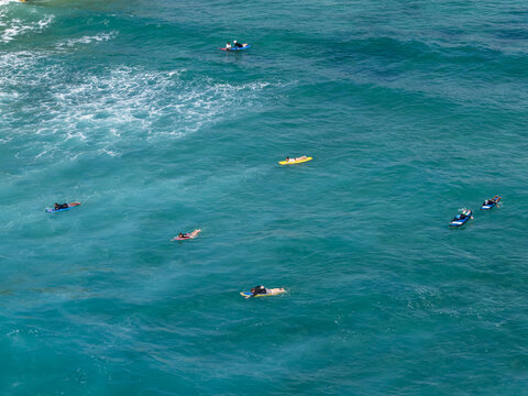 Aerial view of surfers paddling on surfboards in the clear turquoise water of Nusa Dua Beach in Kecamatan Kuta Selatan, Bali, Indonesia.