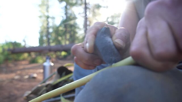 Close up of primitive flintknapped stone blade being used to carve and cut wooden stick outdoors