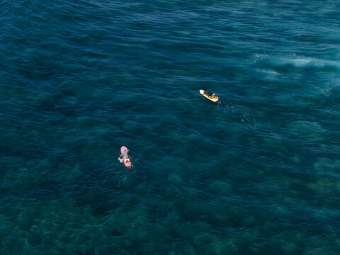 Aerial view of two surfers paddling on their surfboards in the clear turquoise waters at Nusa Dua Beach, Kecamatan Kuta Selatan, Bali, Indonesia.