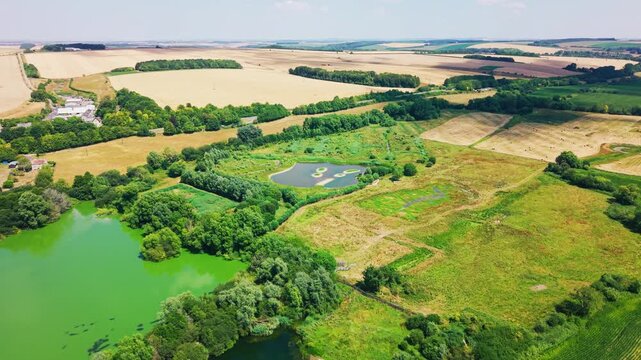 Sweeping drone footage overlooking lakes, restored wetland habitat, nesting islands and surrounding agricultural fields at Langford Lakes Nature Reserve in Wiltshire, England.