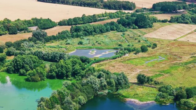 Wide aerial drone footage overlooking interconnected lakes, managed wetland habitat, reedbeds and woodland at Langford Lakes in Wiltshire, England. The elevated landscape shows conservation areas