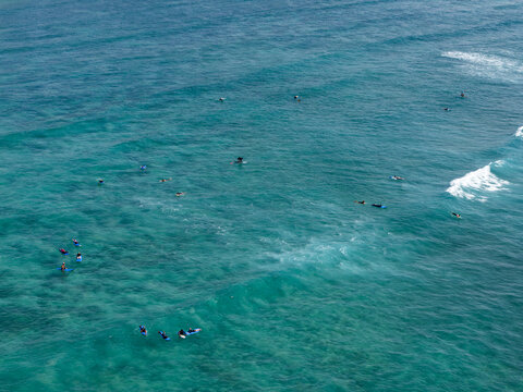 Aerial view of surfers on surfboards in the turquoise waters of Nusa Dua Beach with gentle waves rolling in, Kecamatan Kuta Selatan, Bali, Indonesia.