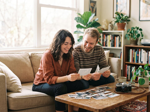 Young couple sitting on sofa looking at printed photographs together at home