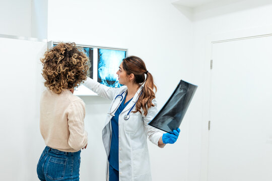 Female doctor and patient reviewing and discussing X-ray scans on a lightbox in a medical office. Healthcare and orthopedic diagnosis concept.