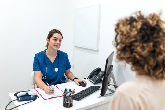 Female doctor sitting at her desk in a modern medical office and writing prescription or notes while consulting a patient. Healthcare and professional medical consultation concept.