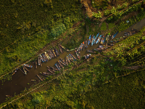Aerial view of Lake Rawa Pening with numerous small wooden boats moored along a narrow waterway, surrounded by lush green vegetation in Waduk Rawapening, Central Java, Indonesia.