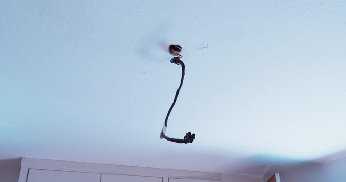 Exposed electrical wires hanging from the ceiling after removing a light fixture. Concept of electrical hazard, home renovation, wiring installation, and electrical safety.