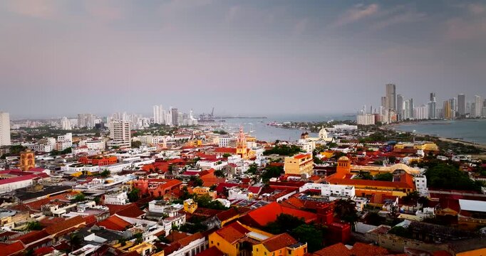 Aerial panorama of Cartagena old town and Caribbean waterfront at sunset, drone descends tilt up under cloudy sky