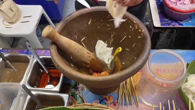 Vendor Mixes Fresh Spicy Thai Papaya Salad (Som Tum), Rice Noodles, & Fried Pork Skin in Mortar & Pestle. Asian Street Food Open Night Bazaar Market, Bangkok Thailand