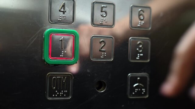 Close-up of persons finger pressing first floor button on metal elevator panel. Button illuminating red after being pushed. Panel has Braille for accessibility. Concept of choice and destination.