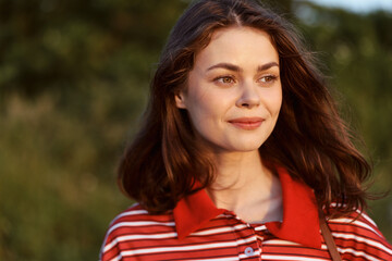 Obraz premium A smiling young woman in a striped shirt enjoys a sunny day at the park. Her lifestyle portrait shows natural beauty, outdoor leisure, happiness, and authentic joy.