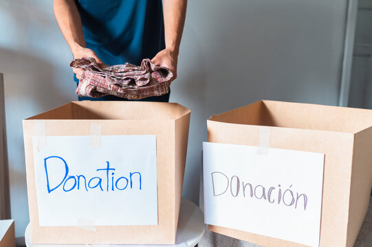 Person placing folded clothes into a cardboard box labeled Donation