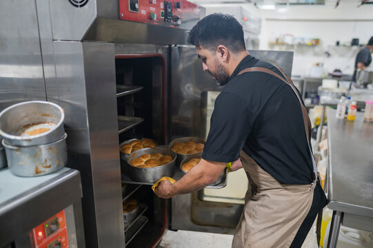 Latino baker putting fresh bread into commercial oven