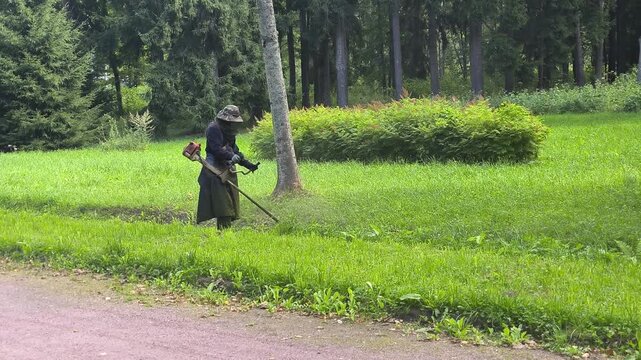 A mower is cutting grass along the road with a string trimmer. 