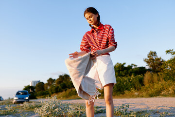 Obraz premium Young woman standing outdoors with a towel celebrating lifestyle during sunset. A person in striped shirt enjoying summer evening in nature. Warm natural light creates a beautiful peaceful mood.
