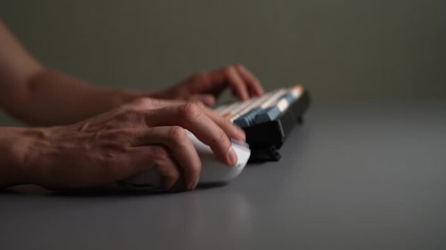 Close-up side view of person hands using white wireless computer mouse with glowing RGB lights and typing on mechanical keyboard. Focus on clicking and scrolling, tech, gaming content, slow motion.