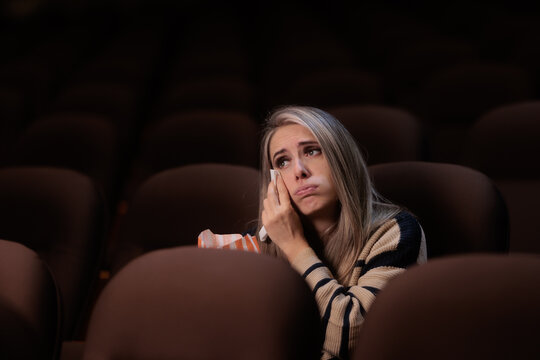 Crying Woman Wiping Tears With Tissue Watching Emotional Cinema Movie. Emotional young female wiping her face while holding popcorn bag in theater