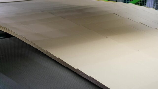 High angle view of neat overlapping brown cardboard sheets moving continuously along a conveyor belt system in industrial manufacturing plant.