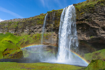 Scenic view of the famous Seljalandsfoss waterfall cascading down green cliffs with a vibrant rainbow in Iceland. © twabian