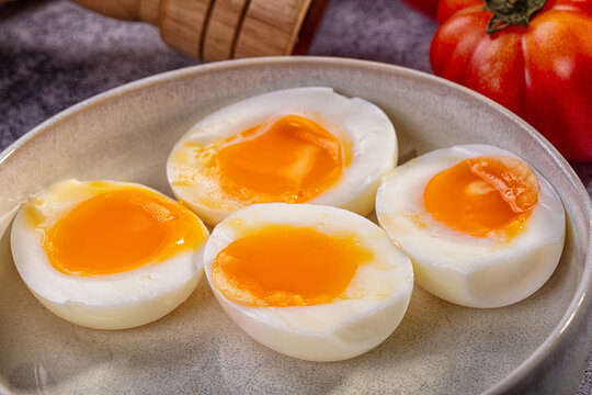 Four halves of soft boiled eggs with runny yolks in ceramic bowl beside tomato