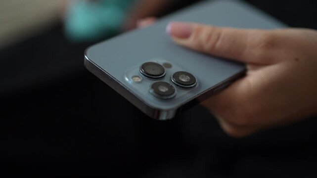 Woman hand wiping dust and fingerprints from modern smartphone triple camera lens with soft microfiber cloth for maintenance and perfect picture quality. Concept of maintenance modern appliance.