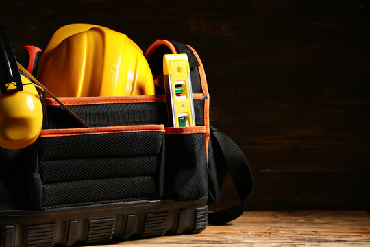 Tool bag with hardhat and construction tools on wooden background, closeup