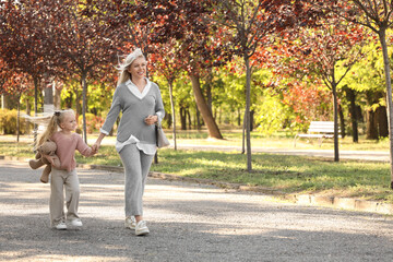 Fototapeta premium Cute little girl with toy bear and her mother walking in park on autumn day