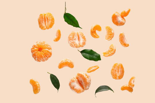 Flying sweet peeled mandarins and leaves on beige background