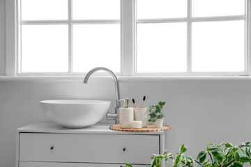 Fototapeta premium Cosmetic products with toothbrushes and houseplant near sink in bathroom