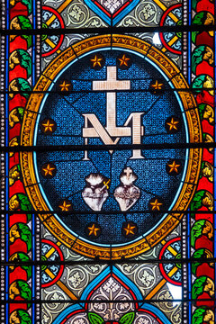 Catholic stained glass showing cross, Marian monogram and Two Sacred Hearts.