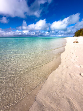 Clear shallow tropical water meeting a white sandy beach beneath a blue cloudy sky at Heron Island, Queensland, Australia.