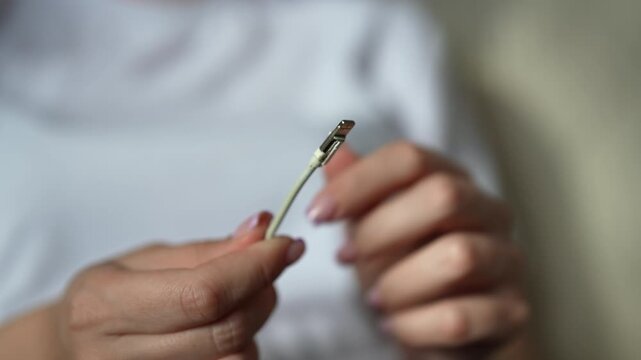 Female hands holding broken and frayed charging cord for smartphone. Concept of issue of electronic waste and need for durable accessories for modern digital devices, close-up, slow motion.