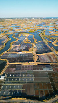 Aerial view of the Marais salants de Guerande featuring geometric salt pans, water channels, and earthen paths under a clear sky in Guerande, Pays de la Loire, France.