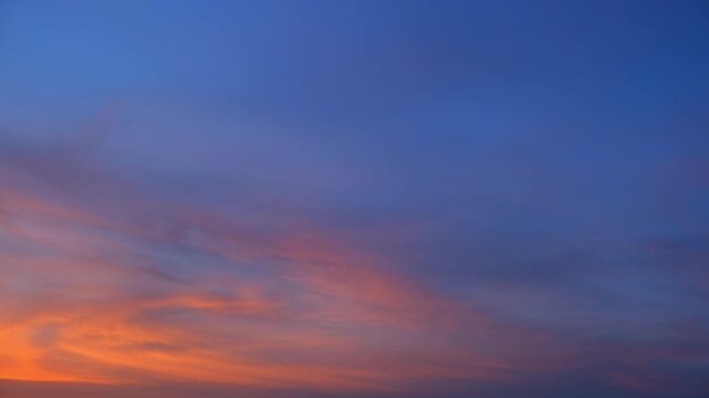 A sunset sky timelapse video featuring dramatic wispy cirrus and thin cirrostratus clouds illuminated by fiery orange sunset light, gradually shifting into soft purple and deep blue evening tones. 4k.