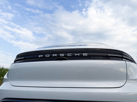 Rear view of a white porsche sports car with logo against blue sky and clouds, low angle close view.
