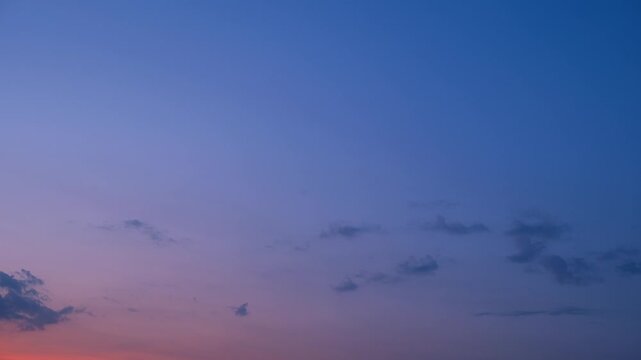 A sunset sky timelapse video featuring an intense pink and violet twilight glow beneath a blue upper sky, with small scattered cumulus clouds moving gently through the peaceful evening atmosphere. 4k.